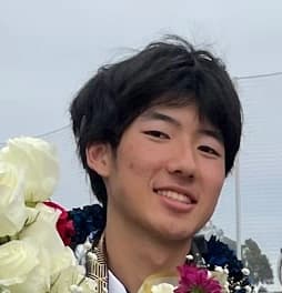 Joshua Yamamoto-Kim smiling at his graduation, holding a bouquet of white roses
